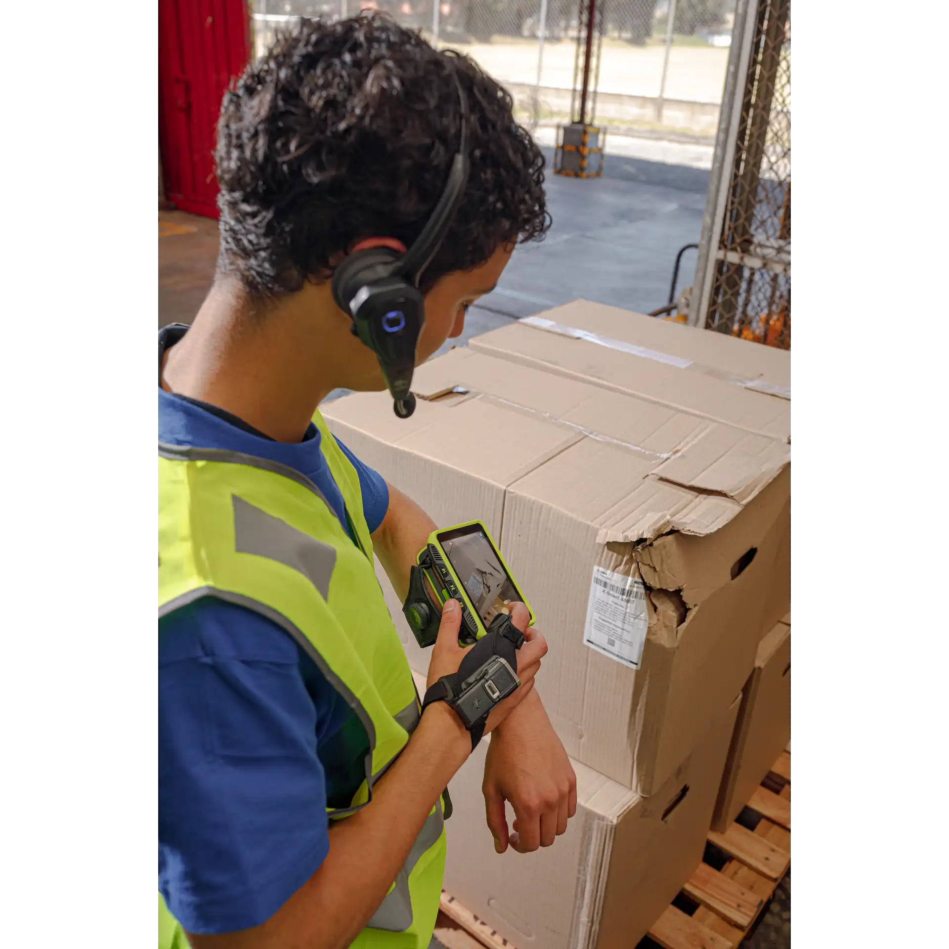 Wearable Zebra WT6400 – seitlich mit RS6100 und eingeschaltetem Display beim Fotografieren eines beschädigten Kartons